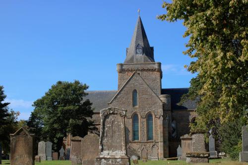an old church with a tall steeple and a cemetery at The Stable Bothy in Rogart