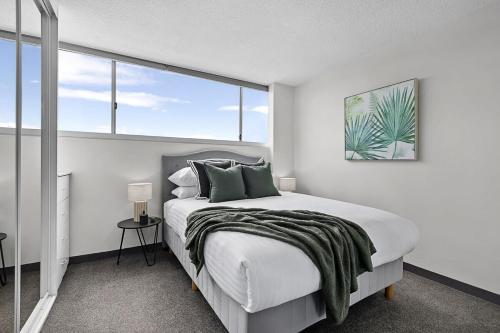 a white bedroom with a large bed with green pillows at Stunning Ocean Views With Manly At Your Doorstep in Sydney