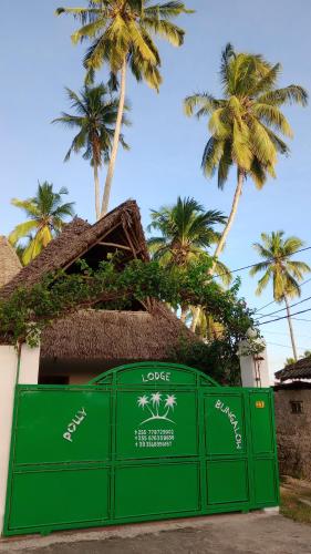 a green fence in front of a building with palm trees at Polly Lodge Bungalow Zanzibar Kiwengwa in Kiwengwa