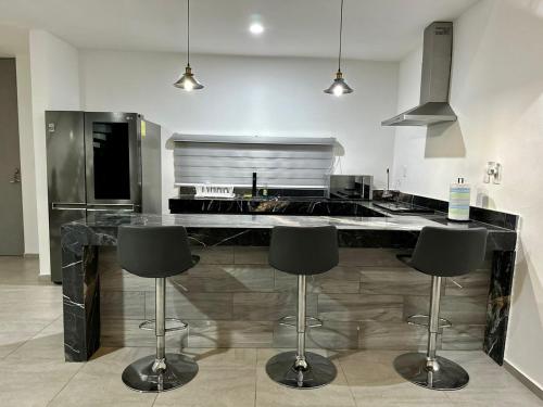 une cuisine avec un comptoir avec quatre tabourets de bar dans l'établissement Casa de 2 Recámaras con Alberca cerca de Plazas Altabrisa, à Mérida