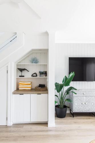 a white living room with a tv and a plant at Sunset Sound Noosa in Noosa Heads
