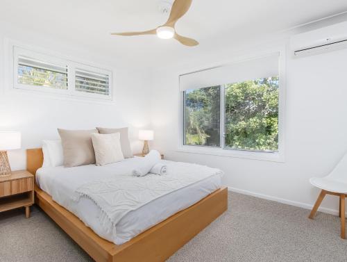 a white bedroom with a bed and two windows at Coastal Home, 500m Walk to Hospital with Ocean Views in Kingscliff