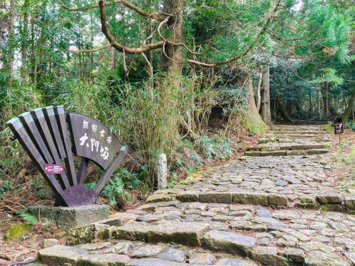 a bench sitting on a stone path in a forest at Kokoyui Guest House in Nachikatsuura
