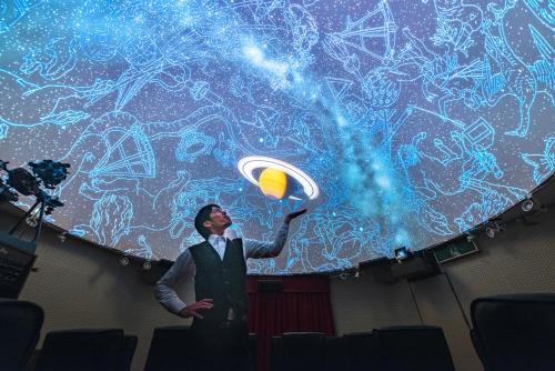 Ein Mann steht vor einer Bühne mit einem beleuchteten Bildschirm. in der Unterkunft Minami Aso Luna Observatory Auberge Mori no Atelier in Minami Aso
