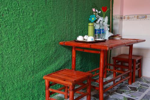 a table with two stools next to a green wall at Cần Thơ Farmstay in Can Tho
