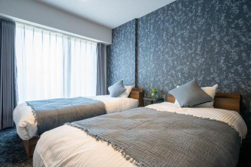two beds in a hotel room with blue wallpaper at MP STYLE Fortuna in Sapporo