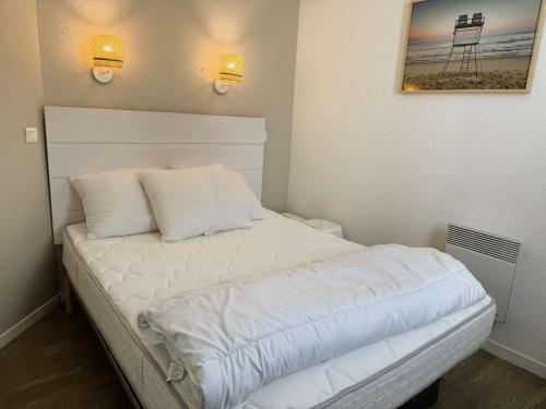 un lit avec des draps blancs et des oreillers dans une chambre dans l'établissement Fouesnant, appartement pieds dans l'eau, vue mer, piscine chauffée, à Fouesnant