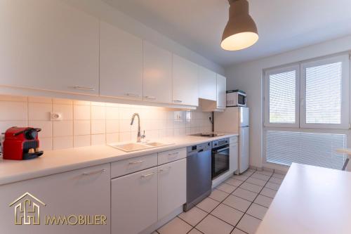 une cuisine avec des armoires blanches, un évier et une fenêtre dans l'établissement L Appart, à Colmar