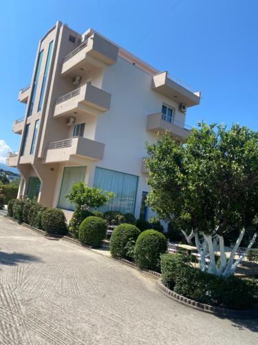 un gran edificio blanco con arbustos delante en Hotel Dini, en Vlorë