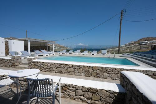 a swimming pool with chairs and a stone wall at Anixi - Primavera Mykonos in Ornos