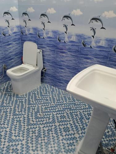 a bathroom with a toilet and a sink and dolphins on the wall at Cherry Binhar, Matogi in Kāta Patthar