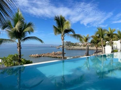 a swimming pool with a view of the ocean and palm trees at Fantastic designer apartment, beachfront! in Bucerías