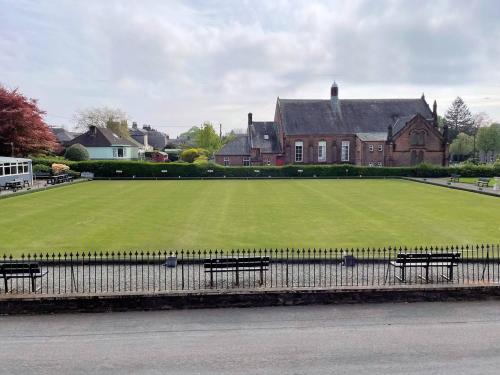 a large green field with benches in front of a house at Pass the Keys Beautiful House With Stunning Views Kirkcudbright in Kirkcudbright