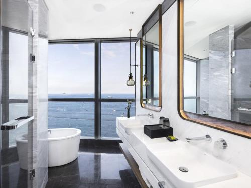 ein Badezimmer mit zwei Waschbecken, einer Badewanne und einem großen Fenster in der Unterkunft 青岛海天大酒店 in Qingdao