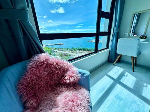 einen rosa Teddybär, der auf einer Couch vor einem Fenster sitzt in der Unterkunft JQ1 SEA & POOL or CITY View WIFI I WASHING MACHINE for Seaview unit I CUCKOO WATER Jesselton Quay by R2 in Kota Kinabalu