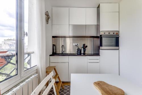 une cuisine avec des placards blancs et une grande fenêtre dans l'établissement Appartement lumineux au dernier étage, à Paris