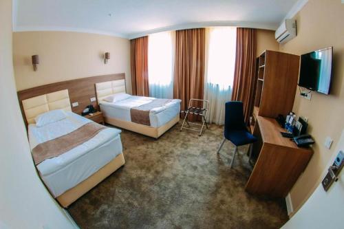 una camera d'albergo con 2 letti e una scrivania di Osh Grand Hotel Chavo a Oš
