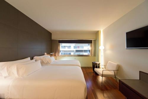 a hotel room with two beds and a flat screen tv at NH Collection Barcelona Constanza in Barcelona