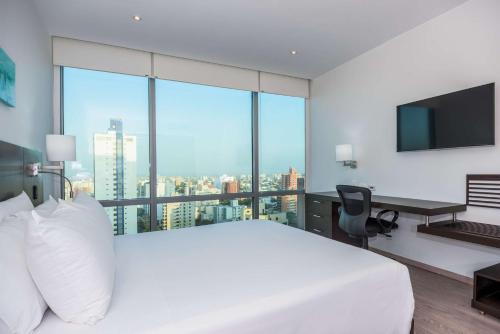 a bedroom with a white bed and a desk with a monitor at NH Collection Royal Smartsuites in Barranquilla