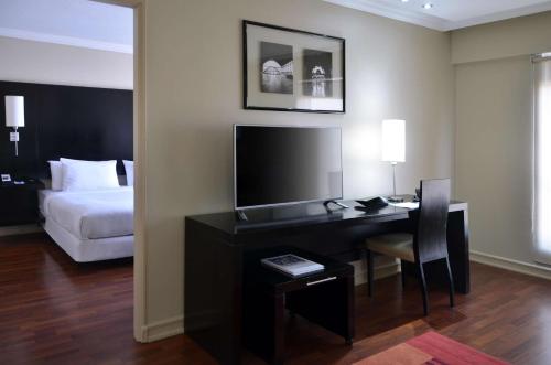 Habitación de hotel con escritorio, TV y cama en NH Ciudad de Santiago en Santiago