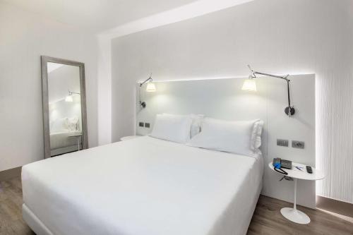 a white bedroom with a large bed and a mirror at NH Milano Congress Centre in Assago