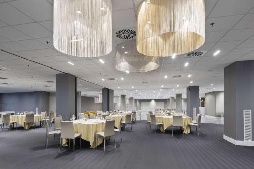 a dining room with tables and chairs and chandeliers at NH Milano Congress Centre in Assago