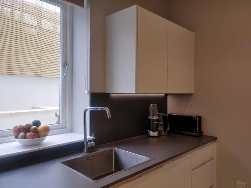 a kitchen with a sink and a window and a bowl of fruit at Luxurious duplex design-flat Kensington in London