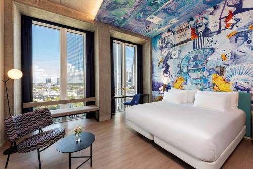 een slaapkamer met een groot wit bed en een muurschildering bij nhow Frankfurt in Frankfurt am Main