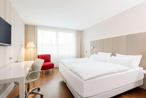 ein Hotelzimmer mit einem großen weißen Bett und einem roten Stuhl in der Unterkunft NH Collection Köln Mediapark in Köln