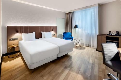 Pokój hotelowy z dużym białym łóżkiem i niebieskim krzesłem w obiekcie NH Luxembourg w Luksemburgu