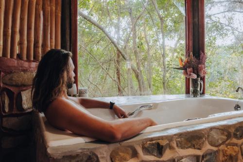 a man sitting in a bath tub looking out a window at Firefly Falls in Plettenberg Bay