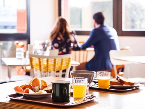 une table avec deux assiettes de nourriture et deux verres de jus d'orange dans l'établissement greet Hotel Beaune, à Beaune