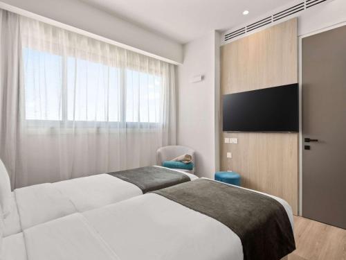 a hotel room with two beds and a flat screen tv at Mercure Larnaca Finikoudes Beach in Larnaka