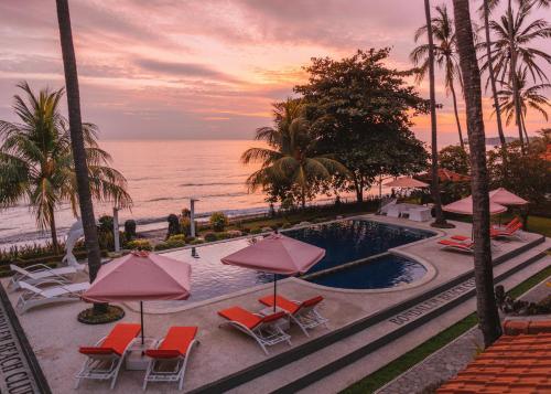 a pool with chairs and umbrellas next to the ocean at Bondalem Beach Club in Tejakula