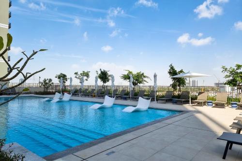 uma piscina num hotel com cadeiras brancas em First Class 1BR Apartment in Dubai Hills - next to Dubai Hills Mall no Dubai