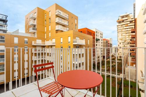une table et une chaise rouges sur un balcon avec des bâtiments dans l'établissement GuestReady - Bel Apt. à Asnières-sur-Seine, à Asnières-sur-Seine