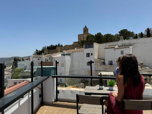 a woman sitting on a balcony looking out at the city at Apartamentos Antequera in Antequera