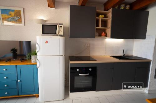 La cuisine est équipée d'un réfrigérateur blanc et de placards bleus. dans l'établissement Appartement climatisé à 100m de la plage, à Vias