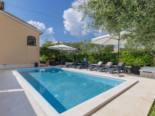 a swimming pool with chairs and umbrellas next to a house at Apartment Mir by Interhome in Vošteni