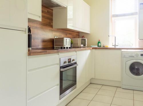 a kitchen with white cabinets and a washer and dryer at Stock Street Apartment in Paisley