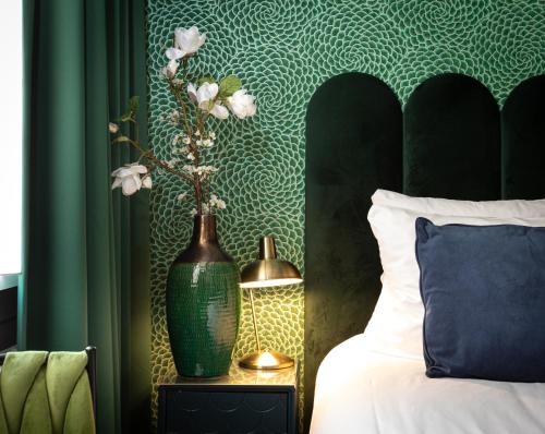 a green vase with flowers on a table next to a bed at Hotel des Arts in Amsterdam