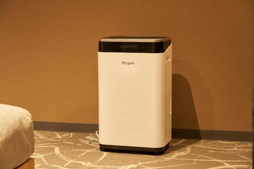 a white and black appliance sitting next to a bed at BbyC Hotel 那覇 レンタカー付ホテル in Naha