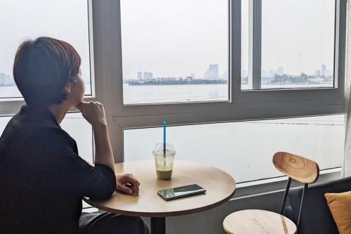 a woman sitting at a table with a drink at Hanoi Home 2 - Lake View Apartment in Hanoi