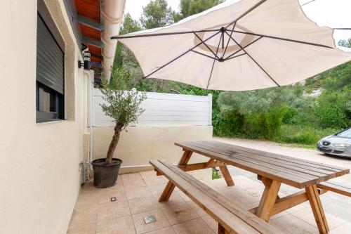 a wooden picnic table with an umbrella on a patio at Gîte rénové Calanque La Vesse in Le Rove