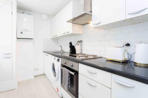 une cuisine avec des placards blancs et un comptoir noir dans l'établissement Sleeps 4 Monthly Discount WIFI Free Parking, à Borehamwood