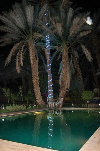 a resort with palm trees and a pool with a lighthouse at Riad Soleil du Monde in Zagora