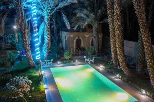 an indoor swimming pool with palm trees and lights at Riad Soleil du Monde in Zagora
