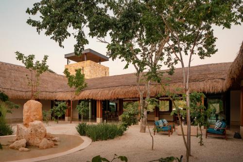 a building with a thatched roof with chairs and trees at Residencia Hacienda Chablé in Chocholá