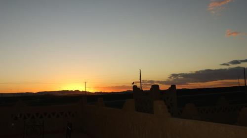 a sunset behind a building with the sun setting in the background at Riad Moha in Merzouga