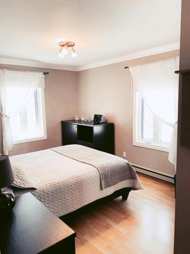 a bedroom with a bed and two windows at À Bon Port in Perce